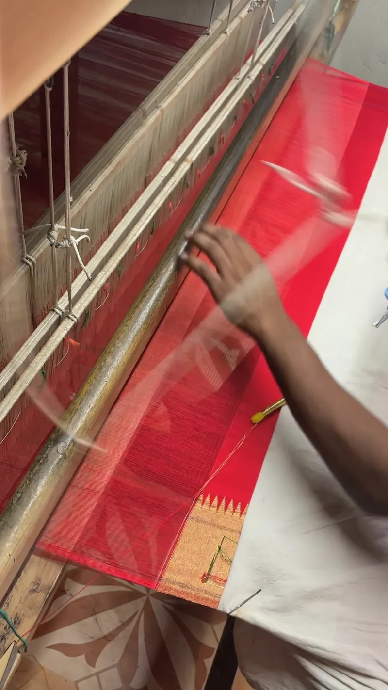 Original video still showing red silk being woven on a traditional handloom